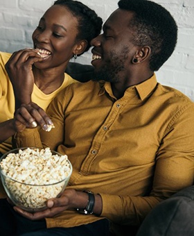 couple eating popcorn while sitting on a couch 