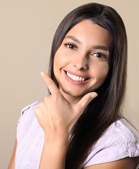 A young female with long, dark hair placing her hand underneath her chin to emphasize her whiter, brighter smile
