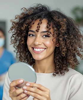 Woman smiling while holding small mirror in treatment room