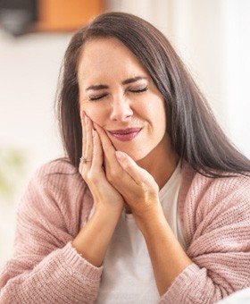 Woman at home holding cheek because of toothache