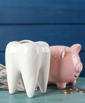 A ceramic tooth model sitting next to a piggy bank and dollar bills