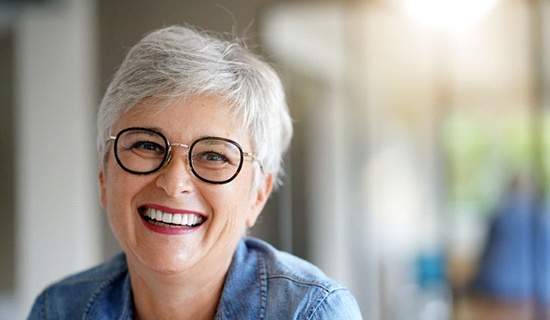 Older woman with glasses smiling with implant dentures in Mangum, OK