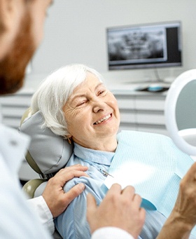 Senior female patient checking her implant dentures in Mangum, OK