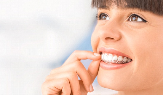 Woman smiling while putting Invisalign trays in