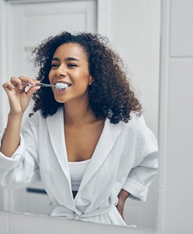 woman in a white bathrobe brushing her teeth 