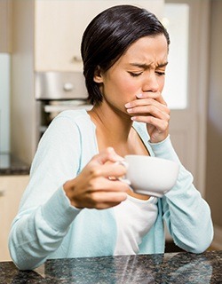 Woman cover her mouth in pain after drinking a sip of hot coffee