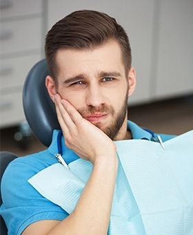 Man in dental chair holding his jaw