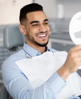 Man holding a handheld mirror and checking smile