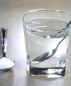 Spoonful of salt next to glass with clear fluid and another spoon