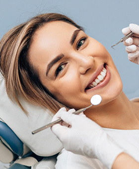 A young woman lying back in a dentist’s chair and smiling while preparing for a checkup