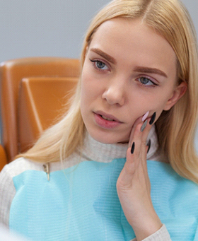 A young female at the dentist’s office holding her cheek in pain and experiencing a dental emergency