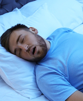 A young man asleep in bed, snoring with his mouth open