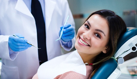 A young woman with dark hair smiling while seated and preparing for a checkup by her dentist near Elk City, OK