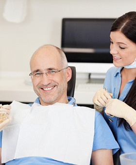 A middle-aged man with glasses listens as his dentist and dental hygienist explain dental implants