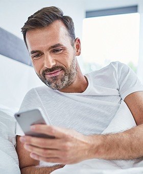 Smiling man in bed looking at his cellphone