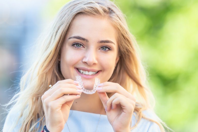 young woman smiling and holding Invisalign aligner